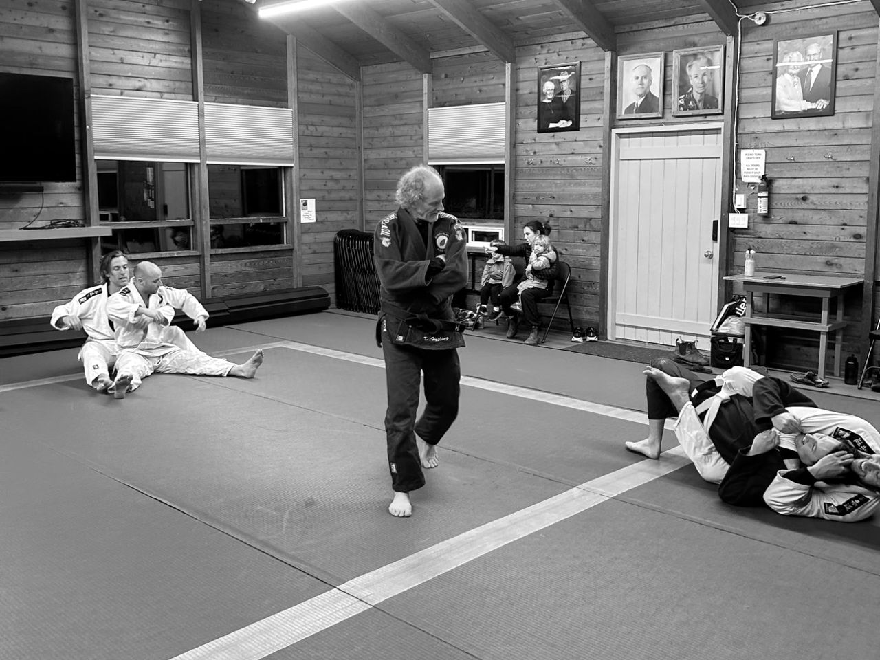 Instructor Dave Hocking, in a blue gi, walks the mat as club members practise on the floor around him