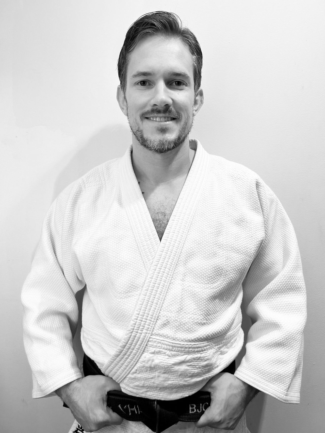 Cohen Hocking smiles in a white judo gi, holding the ends of his black belt