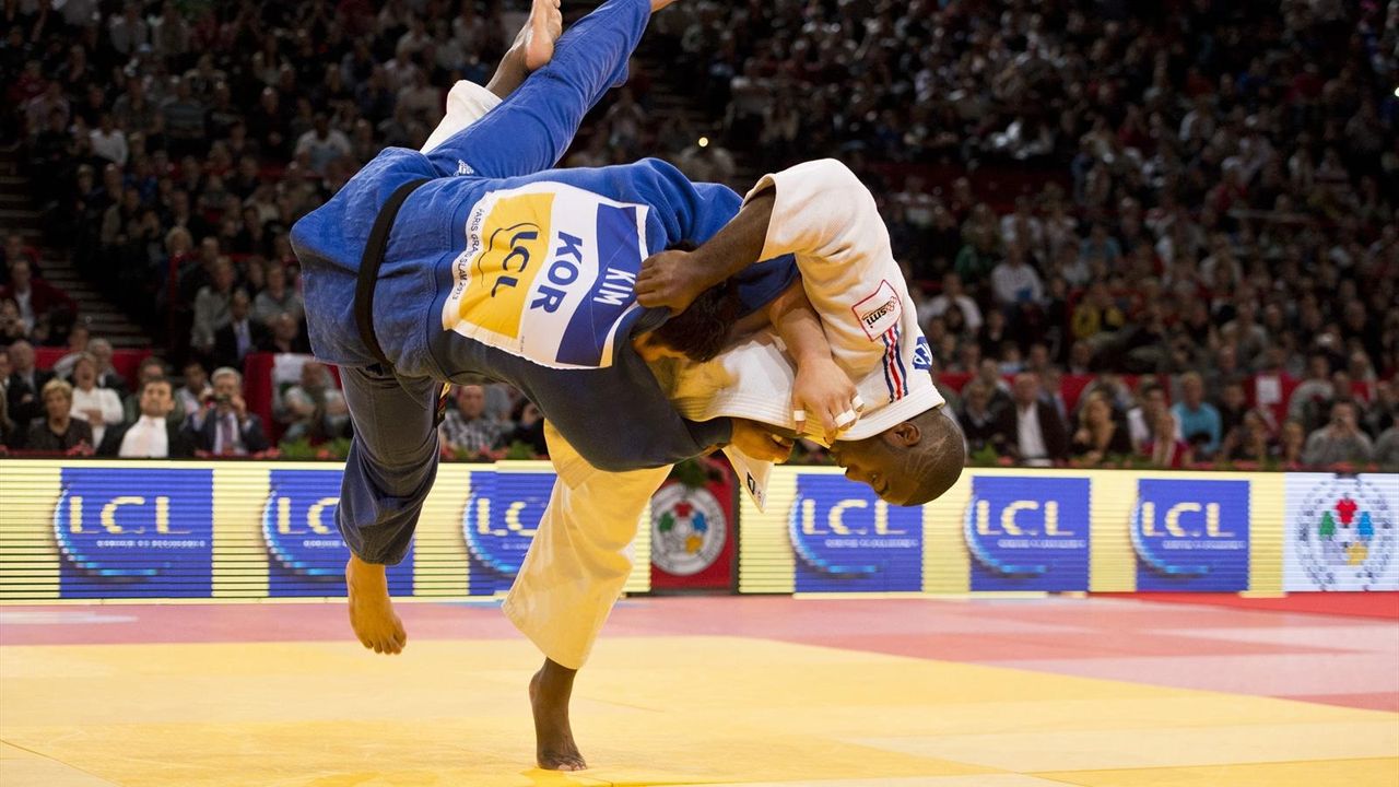 In a packed arena, a judoka in a white gi throws Korea's Kim, in a blue gi, upside down onto the mat