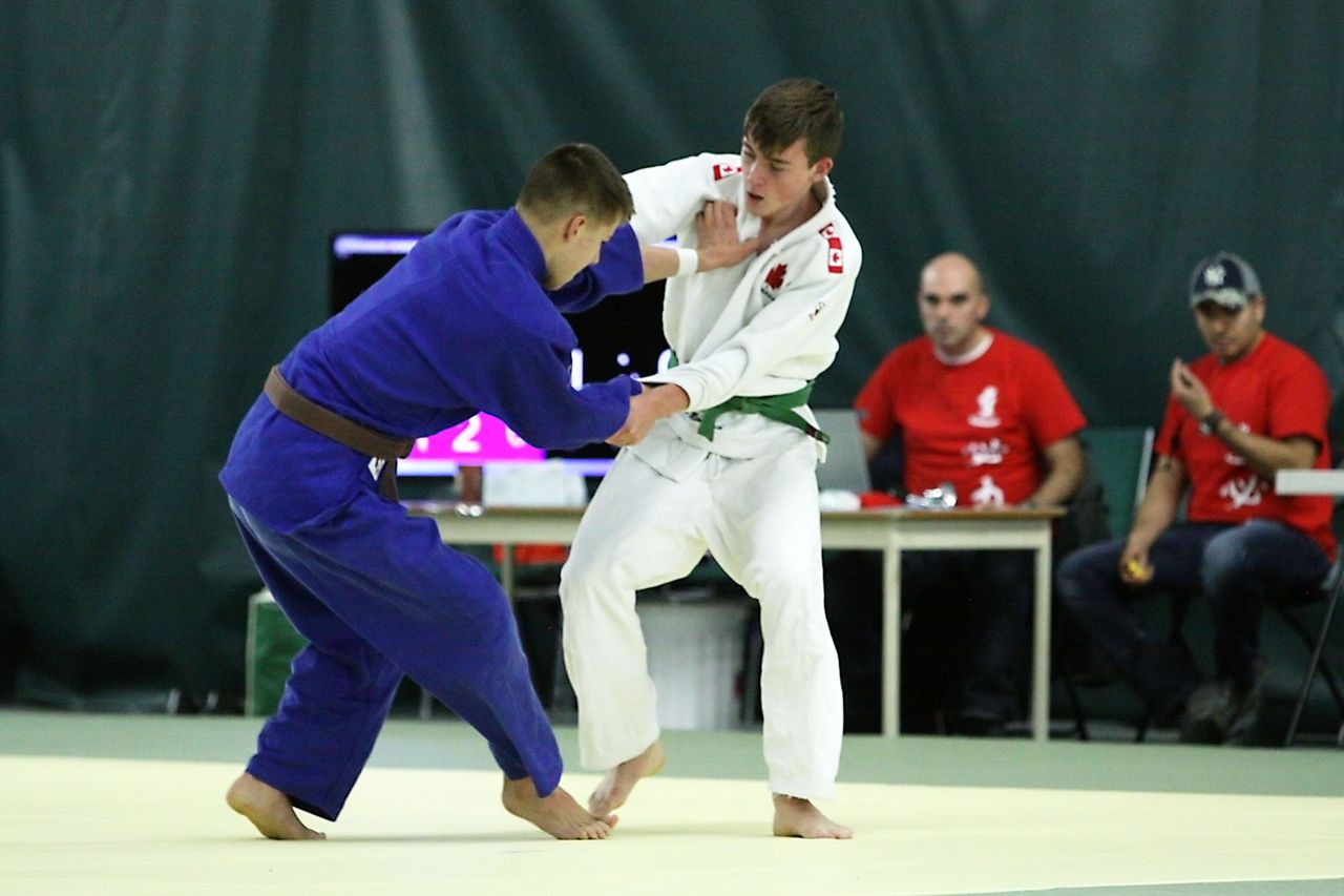 Two teenage judoka, one in a dark gi and one in white, fight for grips during a match